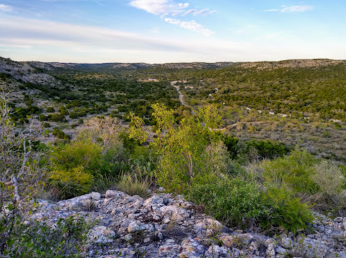 A scenic view of a lush green valley surrounded by rocky hills under a clear blue sky.